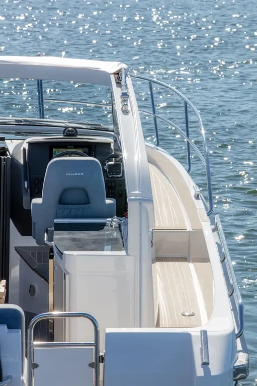 Interior view of a modern boat with a steering wheel, grey seat, and shiny water reflecting sunlight outside.